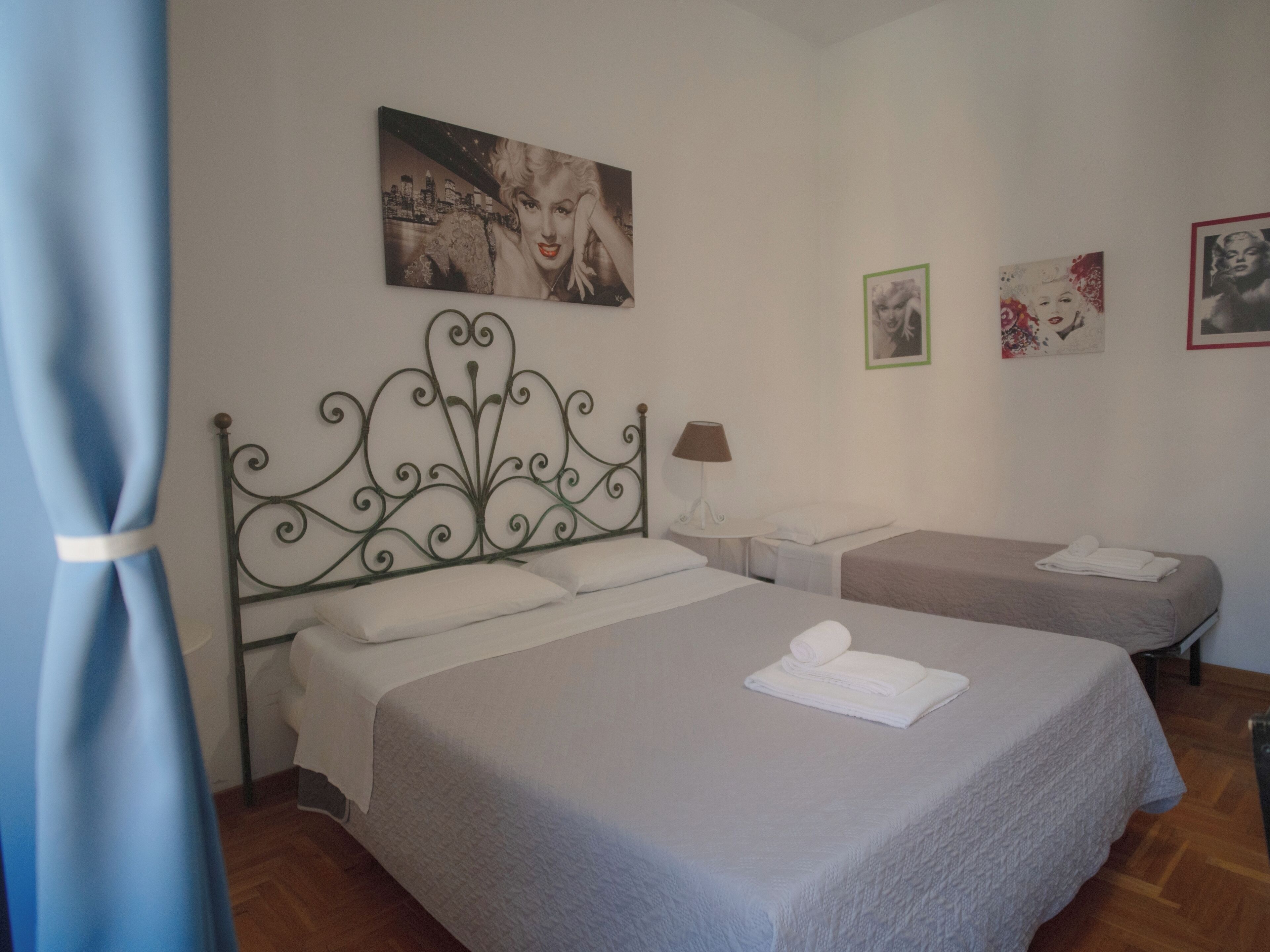 Een hotelkamer met twee bedden, een metalen hoofdeinde, een nachtkastje, een lamp en kunstwerken aan de muren.