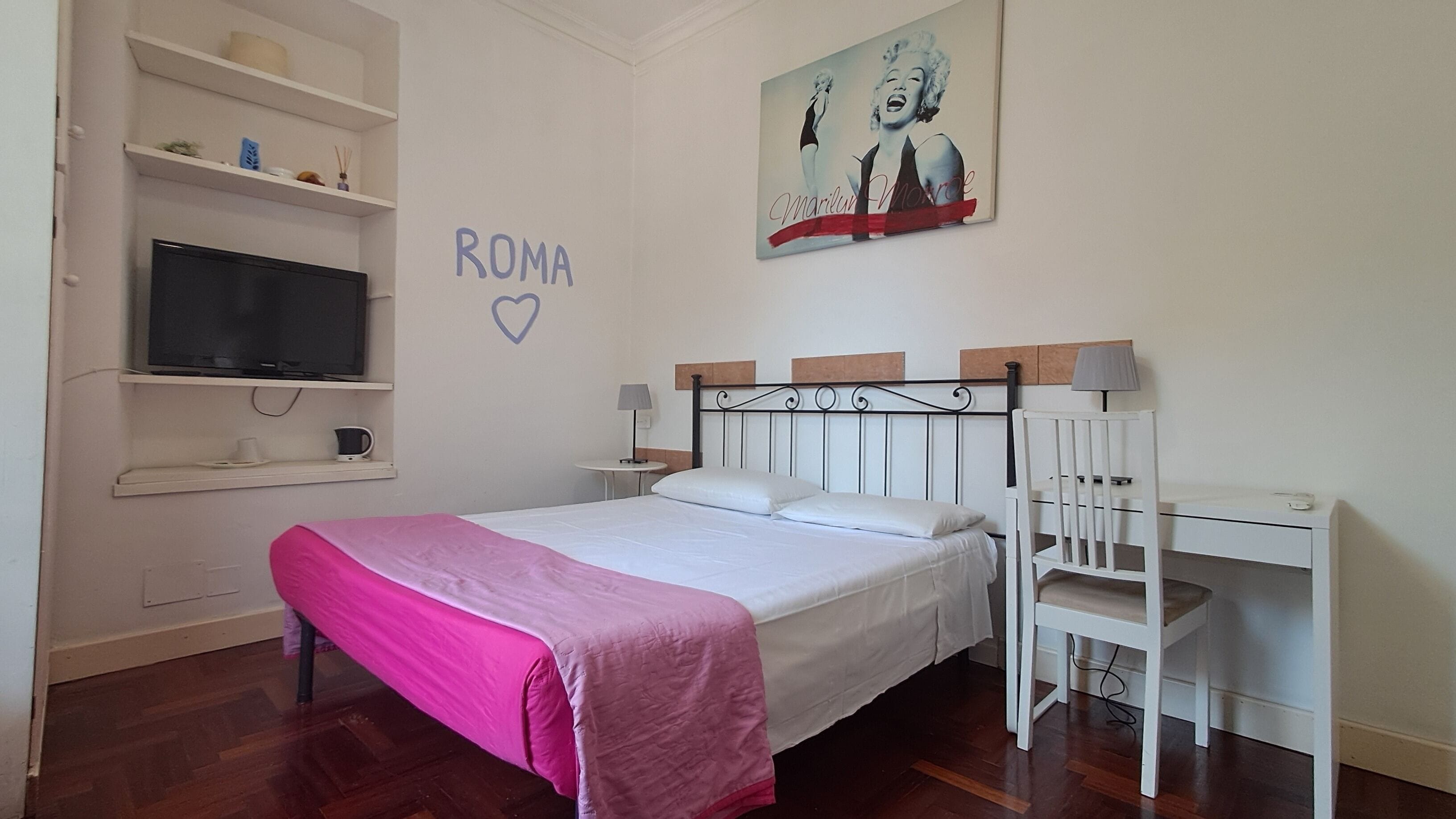Ein Schlafzimmer mit einem Bett, einem Schreibtisch, einem Sessel, einem Fernseher und einem Bild an der Wand.