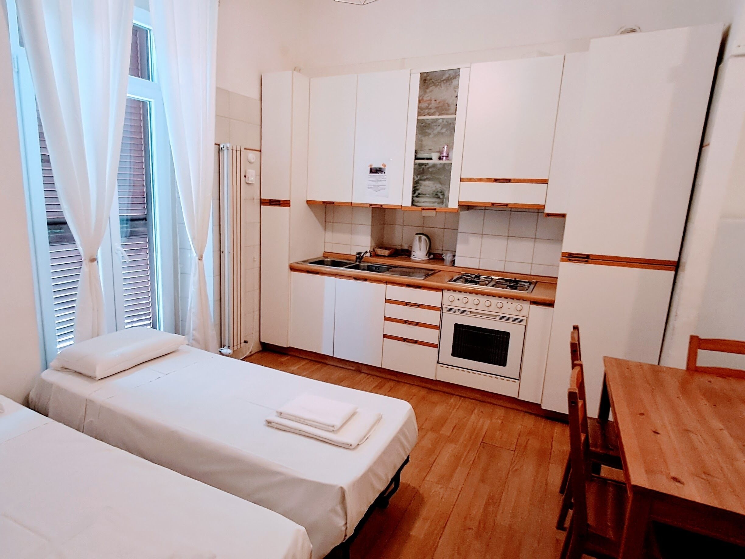 A compact kitchen with a stove, sink, and cabinets, adjacent to a bed with a wooden table and chairs.
