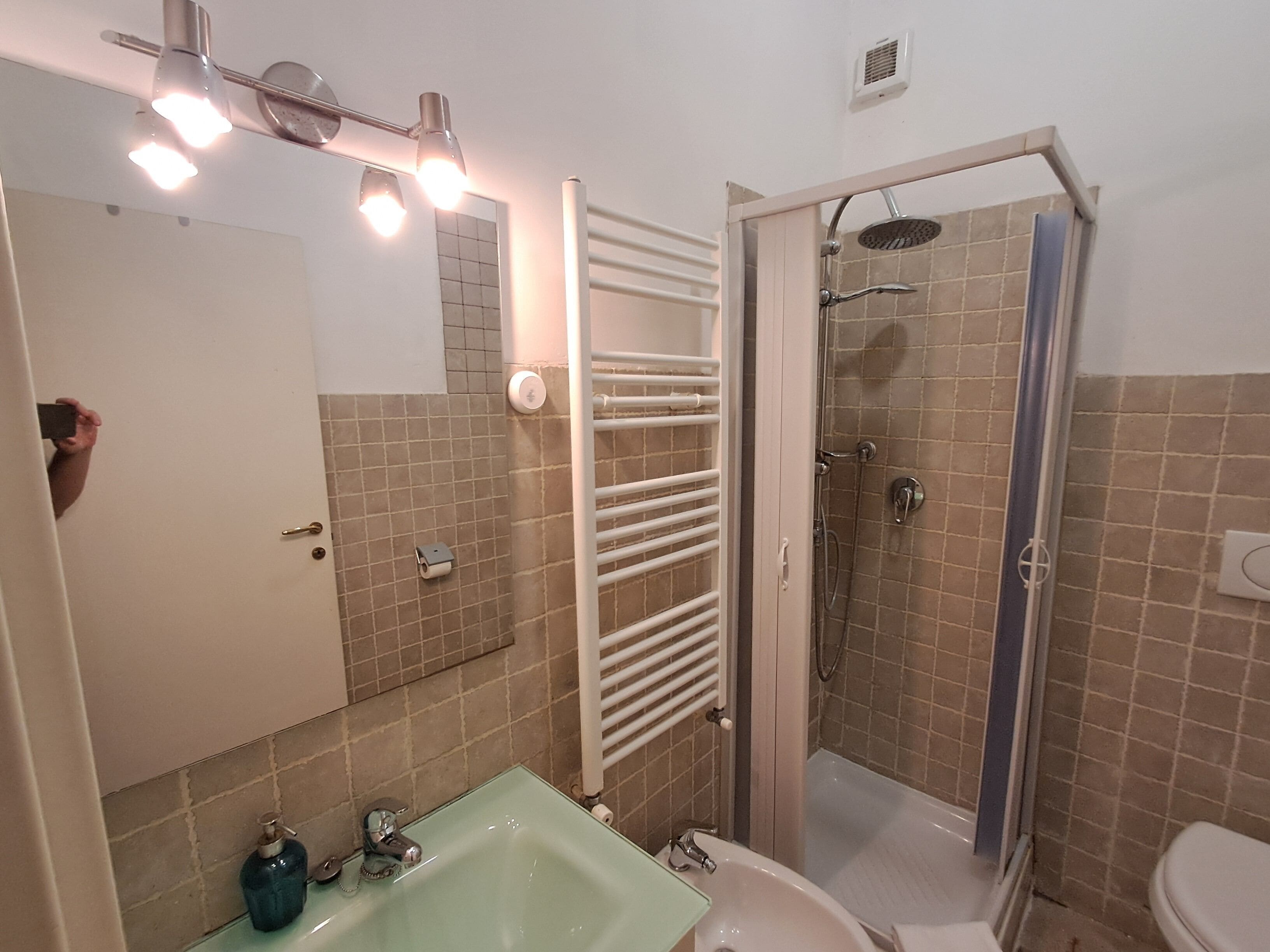 Une salle de bain avec un lavabo en verre, des toilettes, une douche avec une porte en verre et un porte-serviettes.