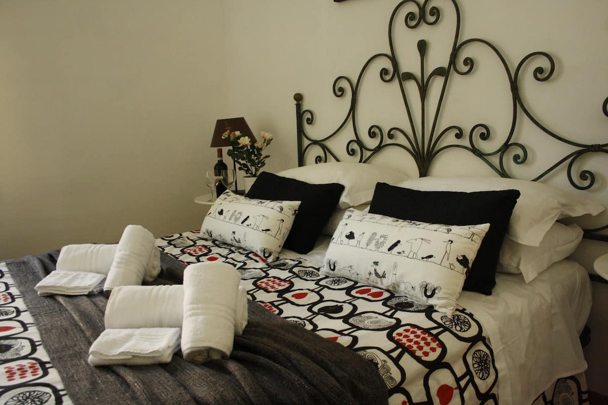 A neatly made bed with patterned bedding, a decorative headboard, and a bedside table with a lamp and flowers.