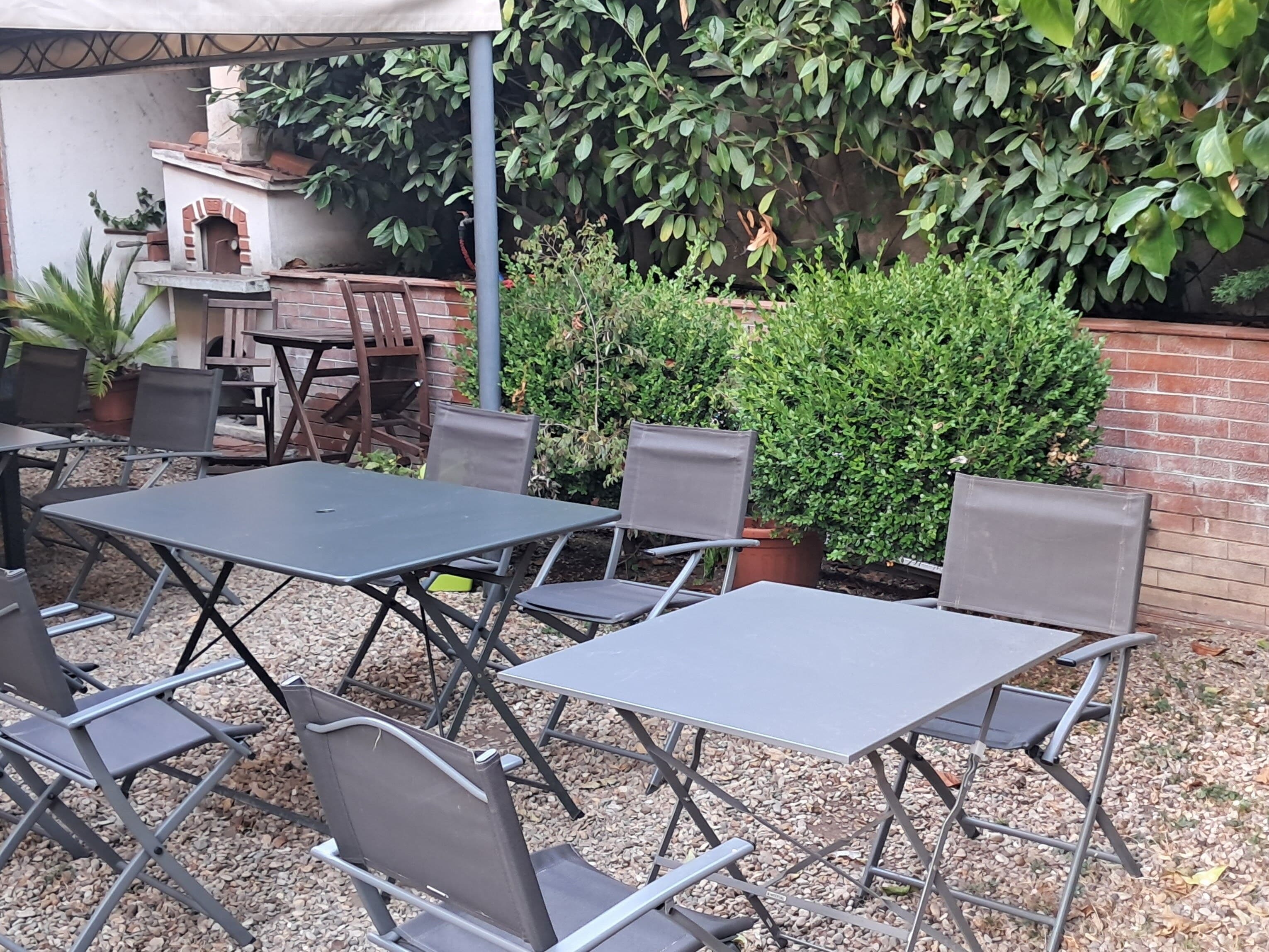 An outdoor patio area with metal tables and chairs, a brick oven, and various potted plants.