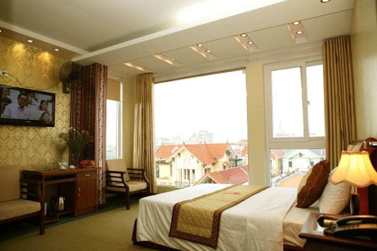 A hotel room with a bed, a desk, a chair, a TV, and a window with a city view.