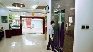 A modern hotel lobby with a marble reception desk, a digital screen, and a glass elevator. - Hoa Lu Hotel 2 (Ninh Binh)