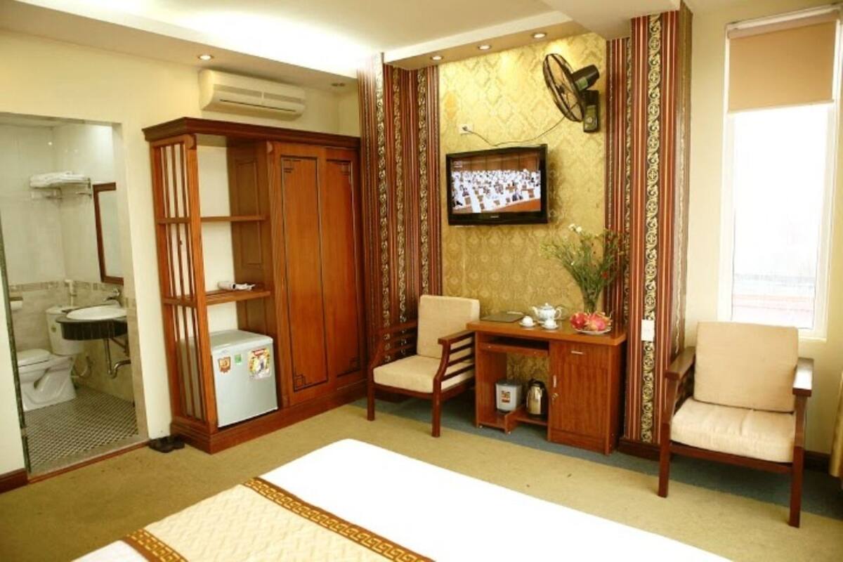 A hotel room with a bed, a wooden wardrobe, a small table with a kettle, a chair, and a television on the wall.