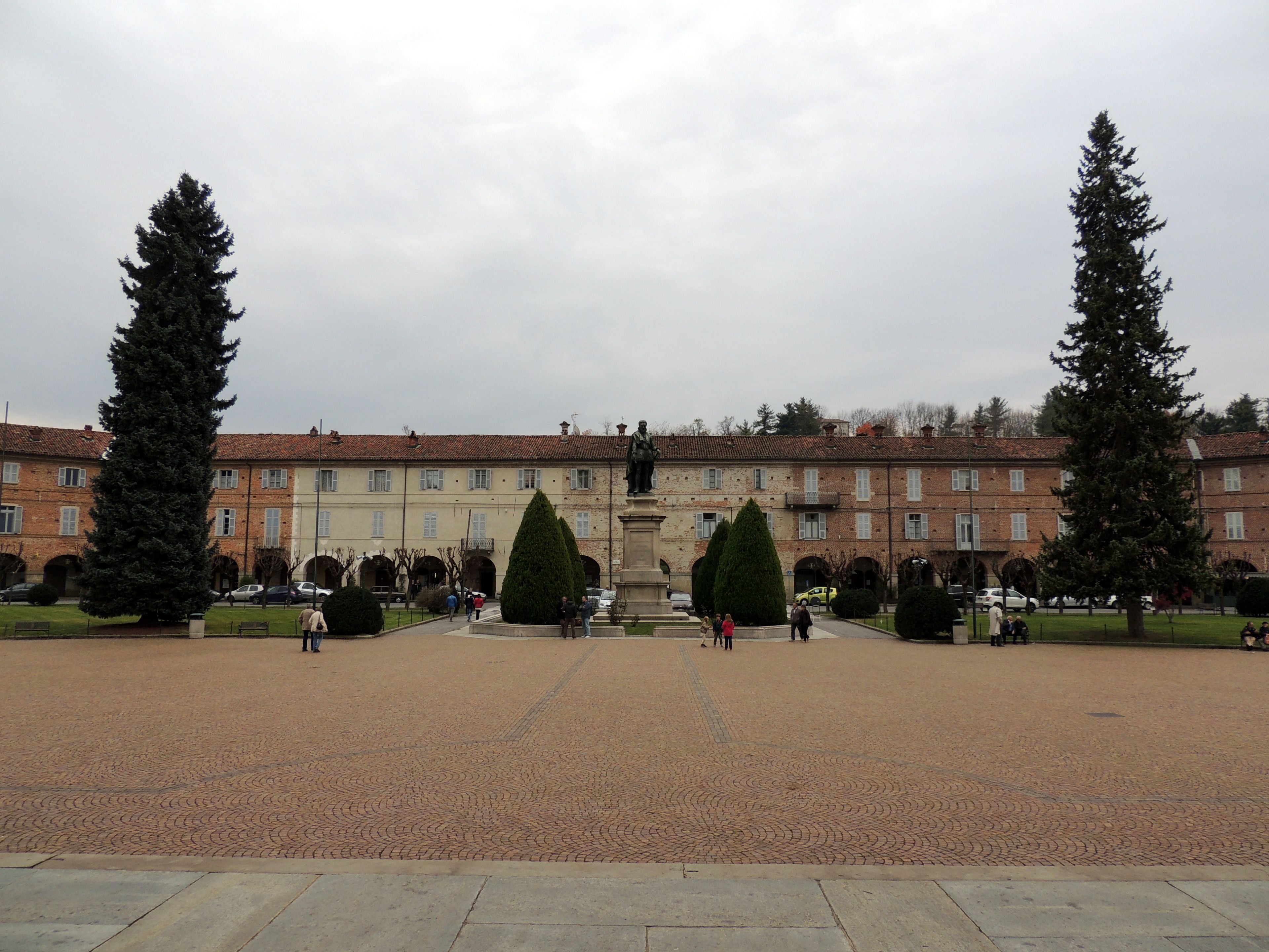 A courtyard with a central statue, surrounded by tall trees and a building with multiple windows.