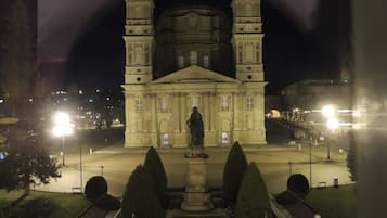 Un edificio grande e histórico con una cúpula central y dos torres, rodeado de un jardín bien cuidado con arbustos podados y una estatua al frente.
