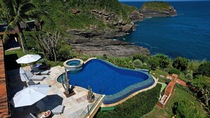 Una piscina de borde curvo, rodeada por un patio con sillones y sombrillas.