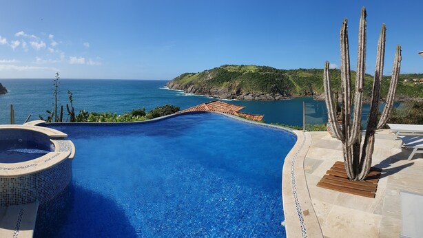 A swimming pool with a hot tub, surrounded by a patio area with cacti and a view of the ocean.