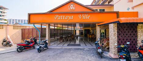 A hotel entrance with a sign reading "Pattaya Ville" and several parked scooters.
