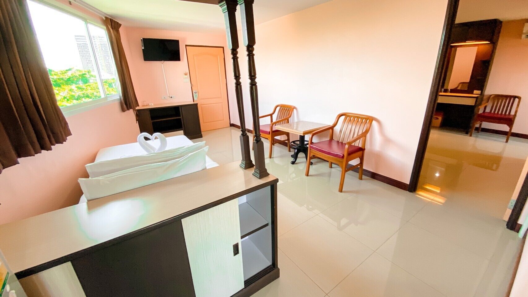 A hotel room with a bed, a desk, a TV, a dining table with chairs, and a view of the outdoors.