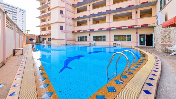 Ein Pool mit Delphin-Motiv, umgeben von einem Gebäude mit mehreren Balkonen und einer gefliesten Terrasse.