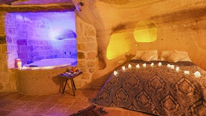 Una habitación acogedora con pared de piedra, una bañera y una cama con velas.