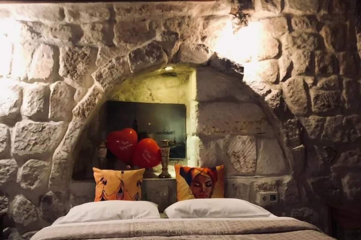 Ein Zimmer mit Steinwänden, einem Bett, Kissen und einem dekorativen Gegenstand an der Wand.