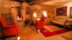 Una habitación acogedora con chimenea de piedra, sillones rojos, alfombra estampada y decoración tradicional.