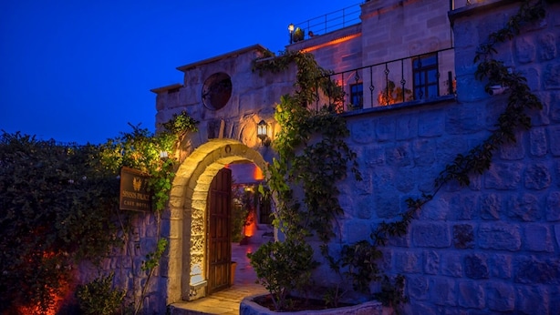 Un edificio de piedra con una entrada en arco, un letrero que dice "Sivasos Palace Cave Hotel" y una escalera que conduce a la entrada.