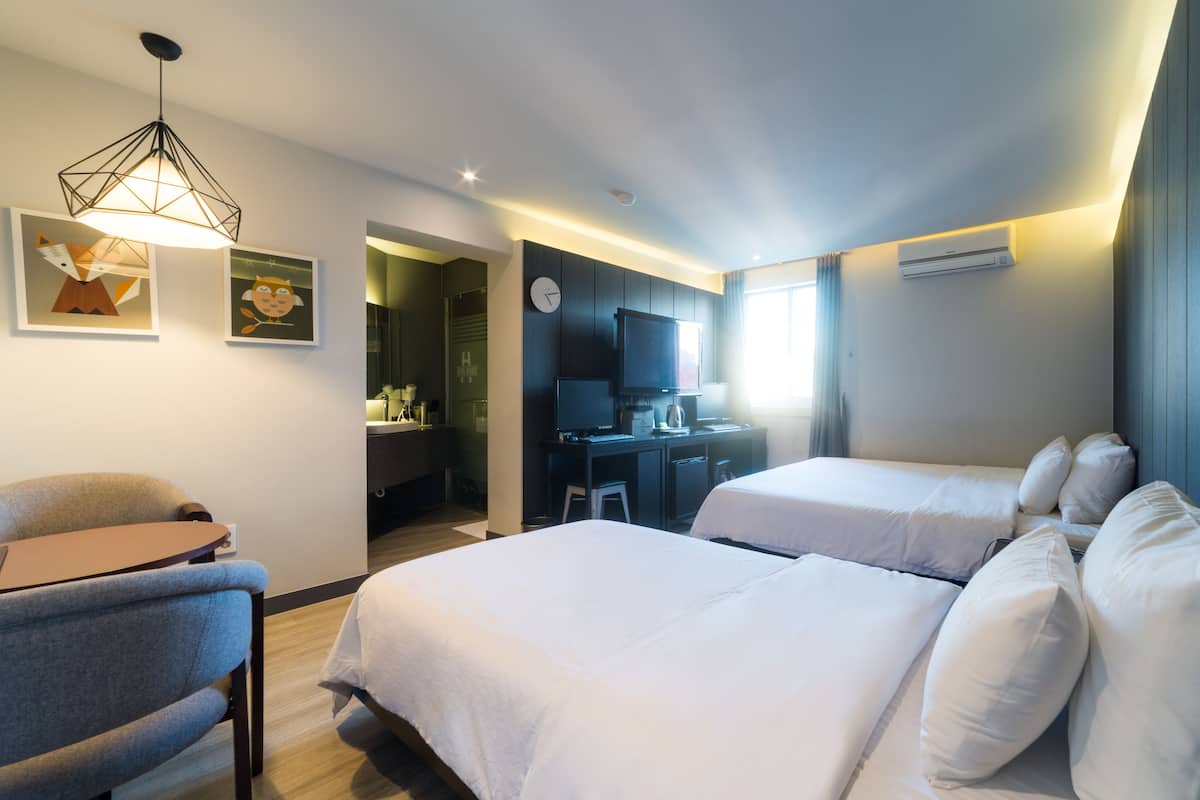 Habitación de hotel con dos camas, un escritorio, una silla, un televisor y obras de arte en la pared.