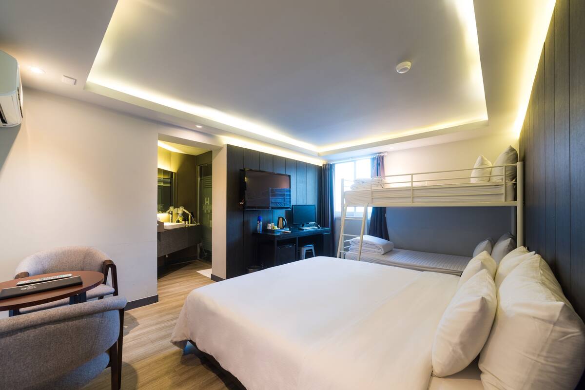 Una habitación de hotel con una cama grande, un escritorio con computadora, una silla y una litera.