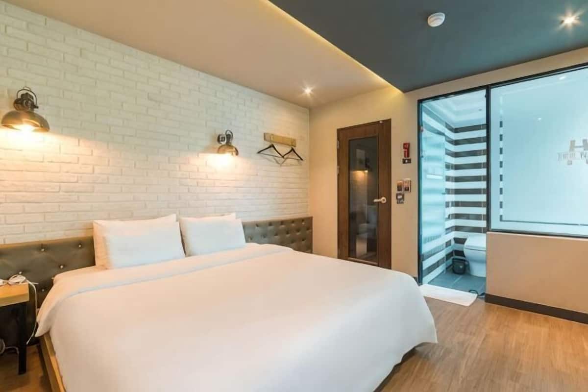 A hotel room with a large bed, a brick wall, a sliding door, and a nightstand.