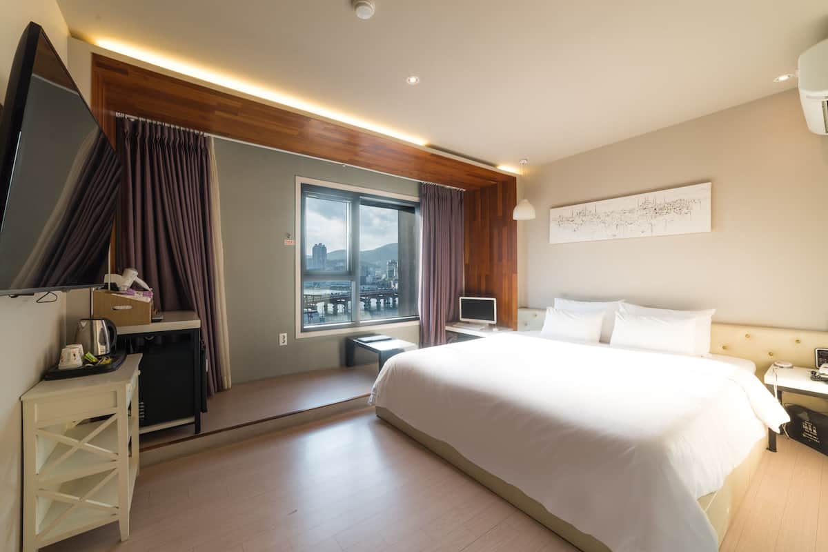 Habitación de hotel con una cama grande, un escritorio con computadora, televisor y ventana con cortinas.