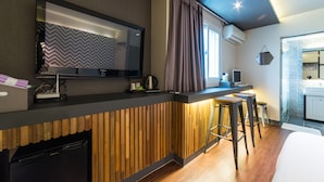 Une chambre d’hôtel moderne avec un mur d’accent en bois, un coin cuisine intégré, un grand miroir et une vue sur la salle de bain.
