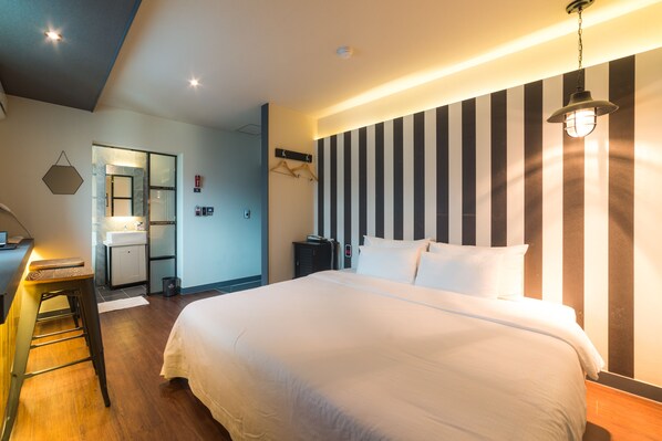 A hotel room with a large bed, a desk with a chair, a mirror, a wardrobe, and a striped wall. - Hotel Bridge (Busan)