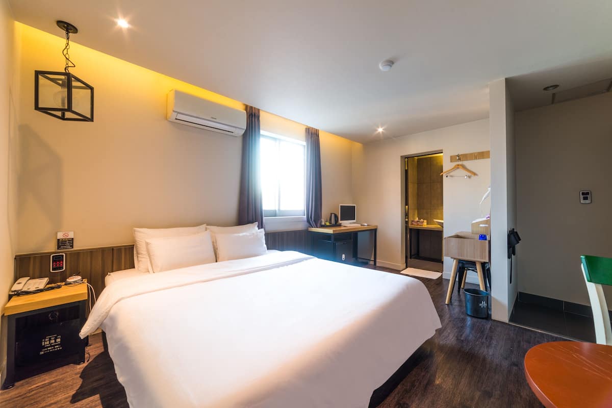 Una habitación de hotel con una cama grande, mesita de noche, escritorio y un espejo.