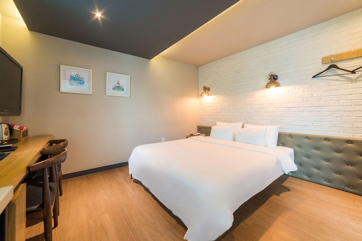 A hotel room with a bed, a desk with chairs, a television, and artwork on the wall.