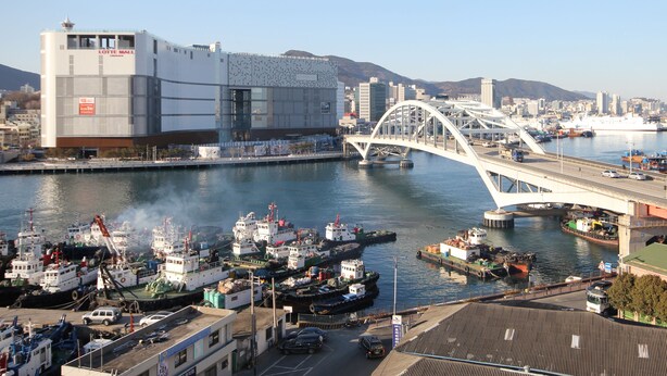 Un port avec des bateaux, un pont et un bâtiment moderne portant une enseigne indiquant « LOTTE MALL ».