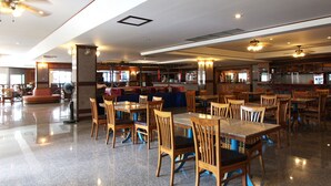 A spacious restaurant with wooden tables and chairs, a bar area, and a ceiling fan.