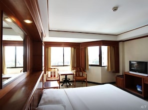 A hotel room with a large bed, a desk with a chair, a television, and a window with curtains. - AA Pattaya Residence (Pattaya)