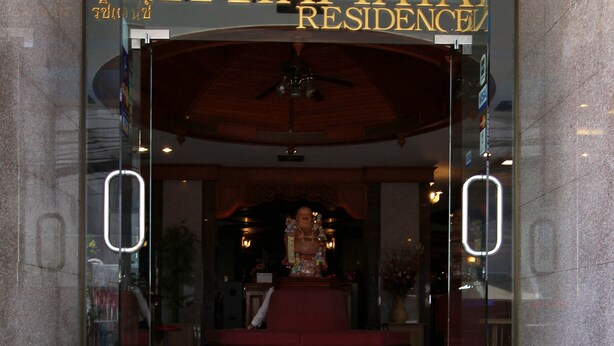 A hotel entrance with a glass door, a ceiling fan, and a statue in the lobby.