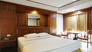 A hotel room with a large bed, a wooden headboard, a bedside table with a phone, and a seating area with chairs and a table.