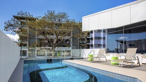A modern outdoor pool area with lounge chairs and a glass balustrade. - Code Apartments (Bowen Hills)