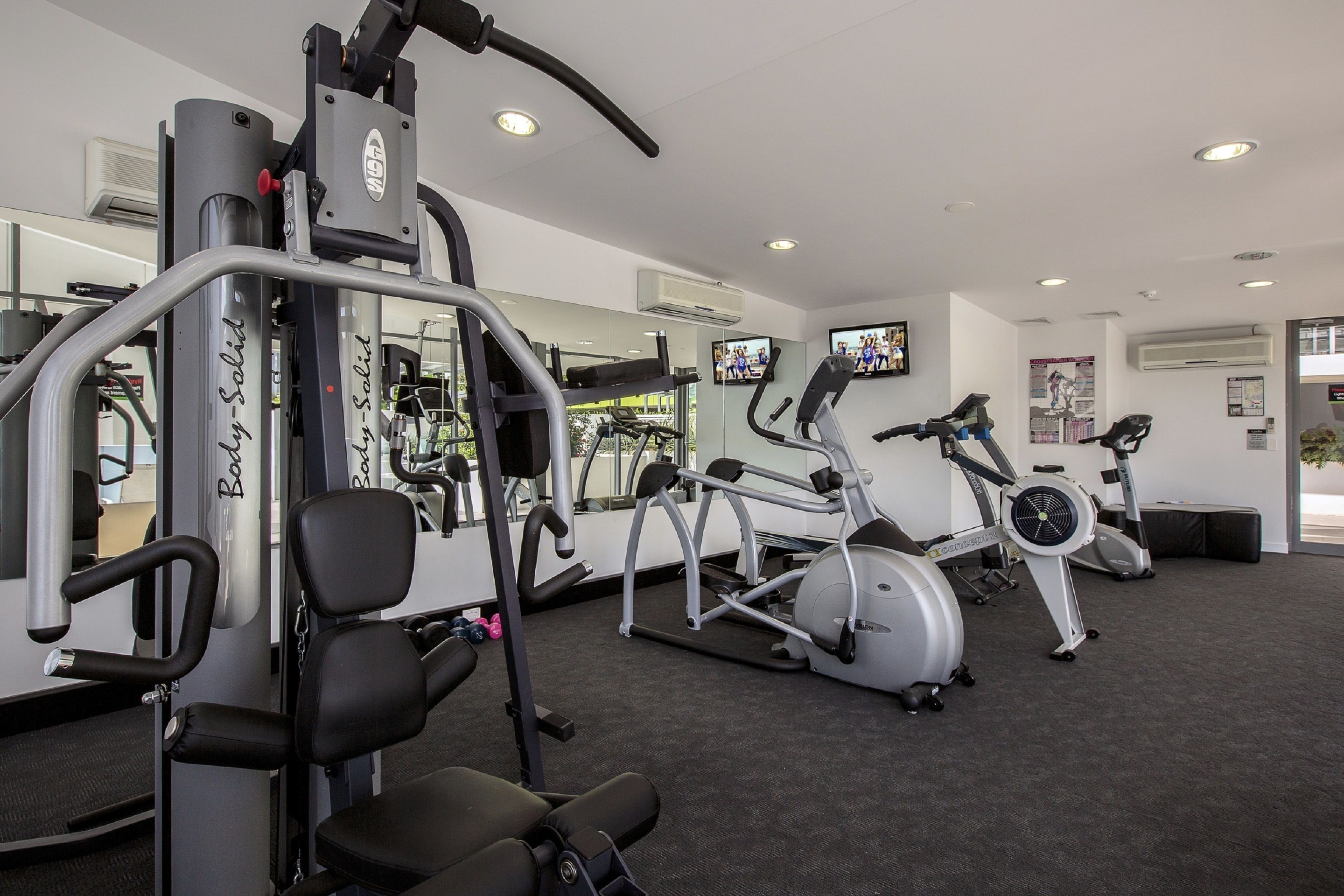 A gym with various exercise machines, a mirrored wall, and a television on the wall.