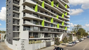 A multi-story building with balconies, a parking area, and a clear sky. - Code Apartments (Bowen Hills)