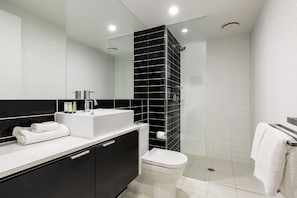 A modern bathroom with a black and white tiled design, a glass shower enclosure, a white sink, and a toilet.