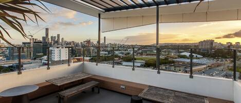 A rooftop terrace with wooden benches and tables, offering a city view.
