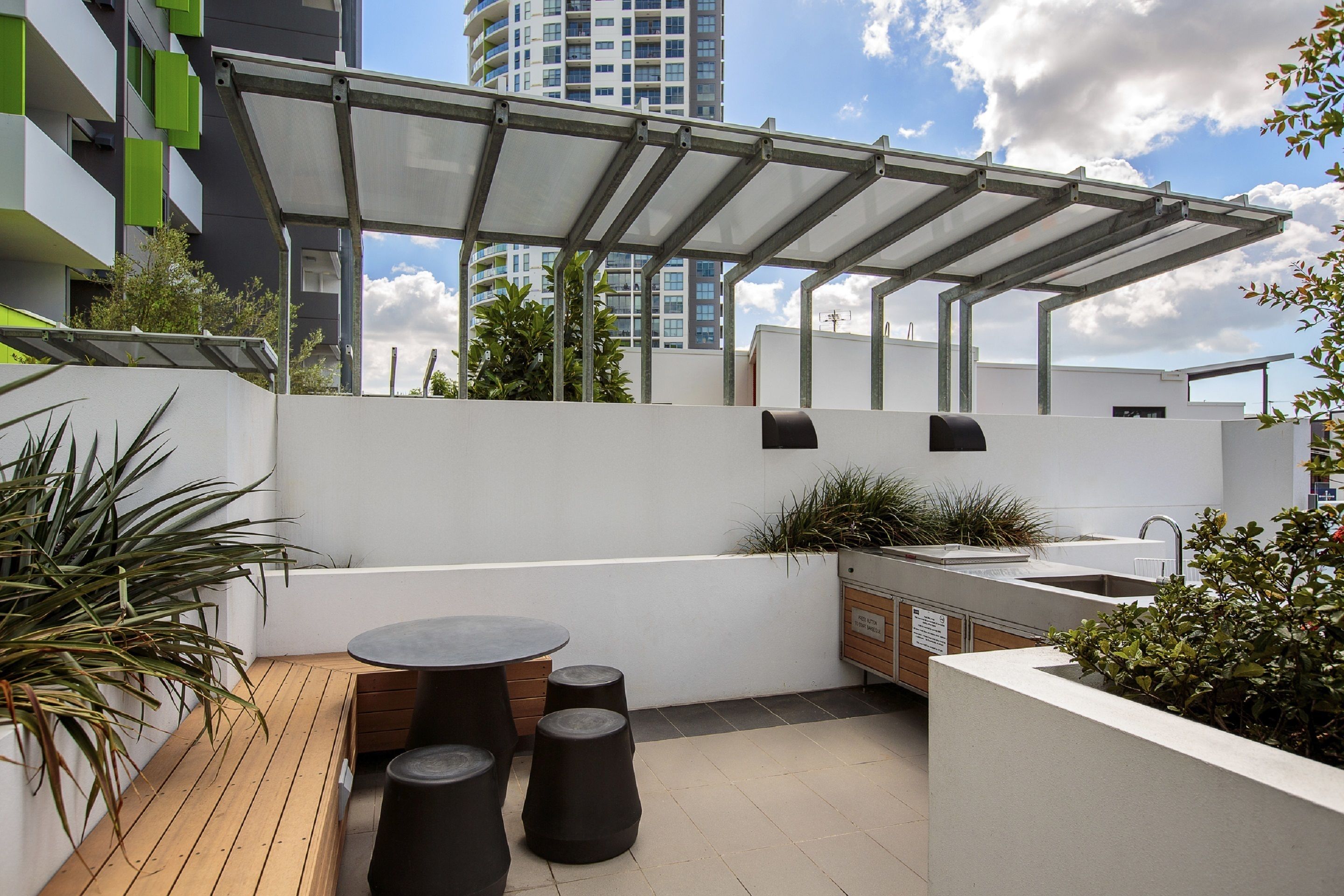 Una terraza en la azotea con pérgola, mobiliario exterior, un lavabo y jardineras.