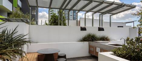 Eine Dachterrasse mit einer Pergola, Sitzgelegenheiten im Freien, einem Spülbecken und Pflanzgefäßen.