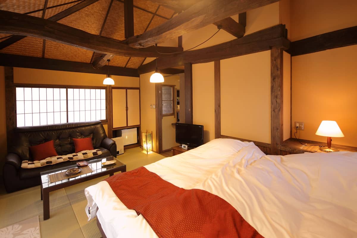 Ein traditioneller japanischer Raum mit Tatami-Böden, einem niedrigen Tisch, einer Couch und einem Bett mit roter Decke.