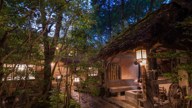 A traditional wooden building with a thatched roof, surrounded by lush greenery and a stone pathway. - Kurokawa Onsen Oyado Noshiyu (Minamioguni)