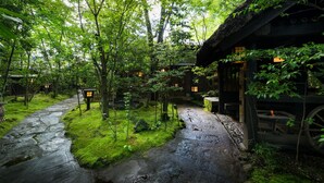 A traditional Japanese-style garden with a stone pathway, wooden structures, and lush greenery. - Kurokawa Onsen Oyado Noshiyu (Minamioguni)