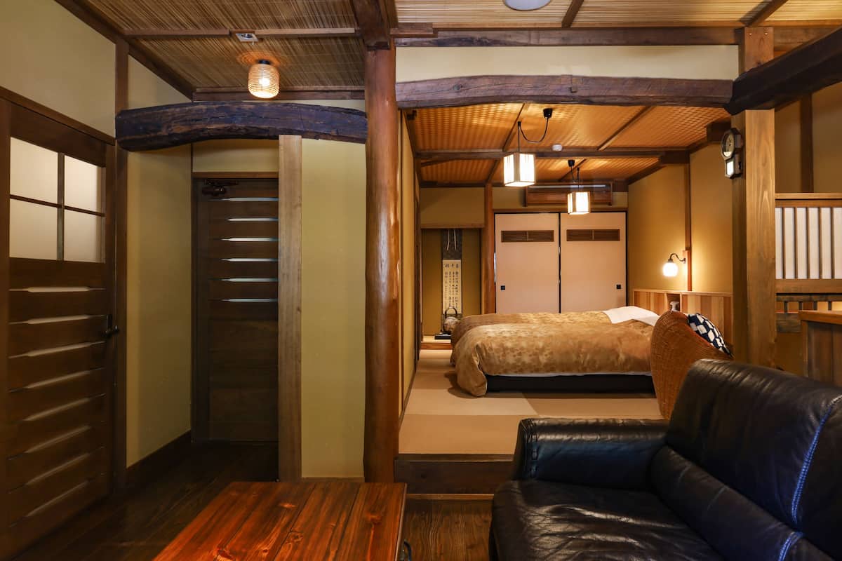 Ein traditioneller japanischer Raum mit Holzboden, einer Couch, einem Bett mit gemustertem Überwurf und einer Schiebetür.