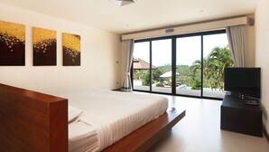 A modern hotel room with a large bed, a flat-screen TV, and a balcony with a view of palm trees. - Baan Napoli Luxury Villa (Koh Samui)