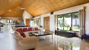A spacious living area with a high ceiling, a glass coffee table, a white sofa with red cushions, and a view of the outdoors through large windows. - Baan Napoli Luxury Villa (Koh Samui)