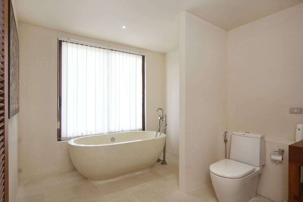A bathroom with a freestanding bathtub, a toilet, and a window with blinds.