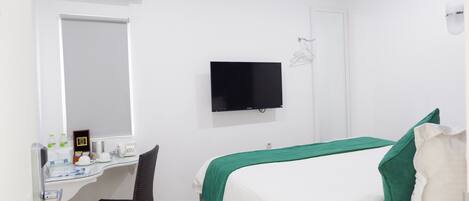 Habitación de hotel con cama, escritorio con silla, televisor de pantalla plana y unidad de aire acondicionado.
