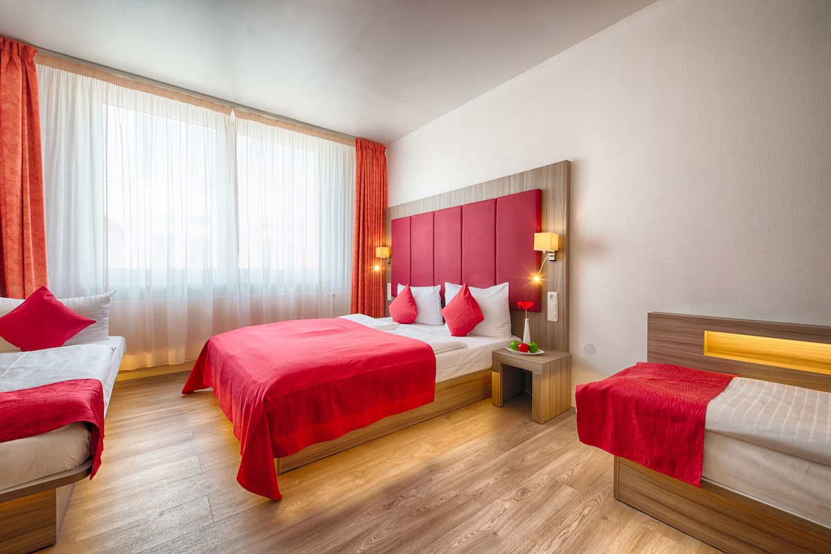 Een hotelkamer met twee bedden, een houten hoofdbord, een nachtkastje en een raam met gordijnen.