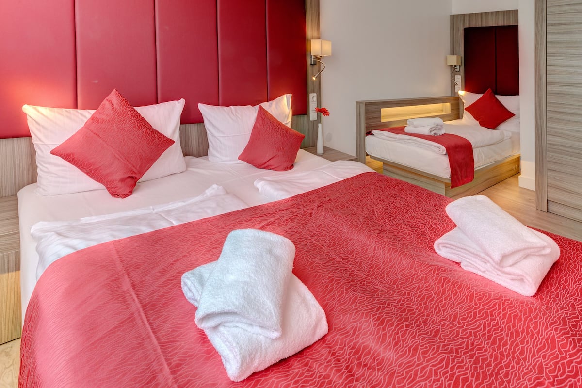 Een hotelkamer met een groot bed, twee kleinere bedden, rode en witte beddengoed, en een rode accentmuur.
